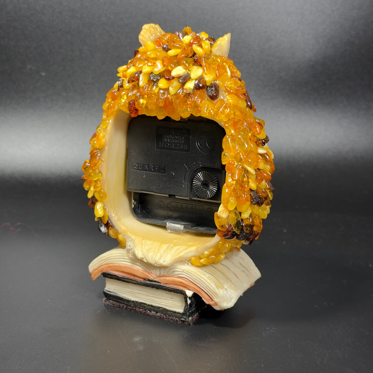 Back of the amber owl clock, covered in honey and brown Baltic amber, with the quartz movement above the book base.