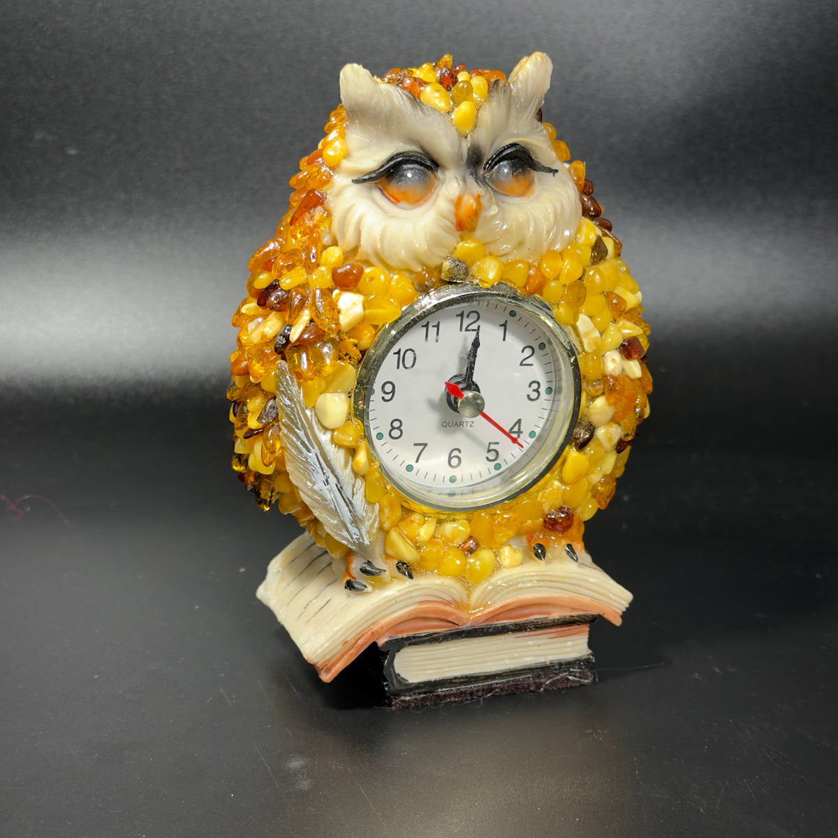 Front photo of the amber owl table clock showing the ivory face, clock dial, silver quill and stacked book base.