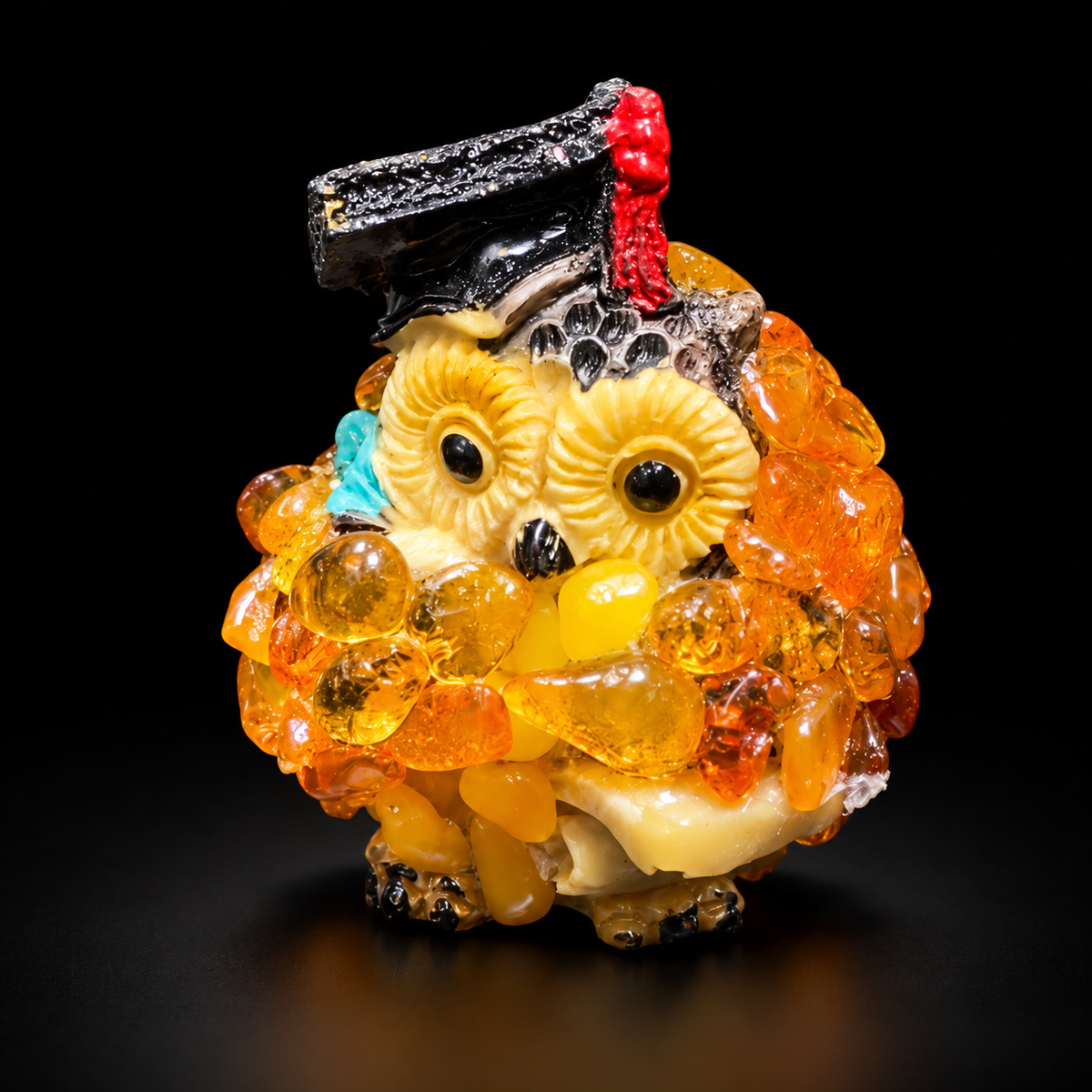 Golden-orange owl figurine with black graduation cap and red tassel on a black studio background