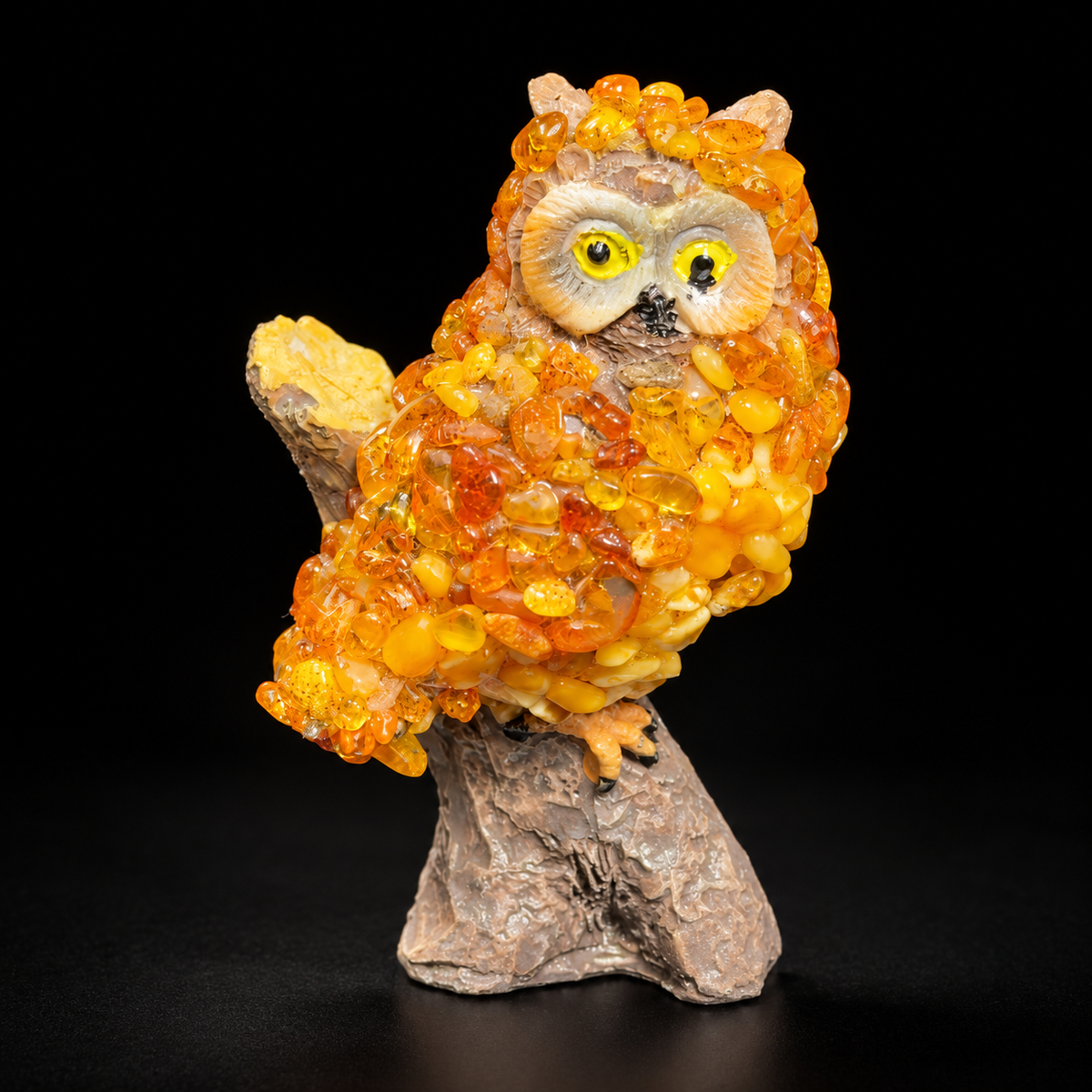 Golden orange owl figurine with yellow eyes and tree stump base on a black studio background