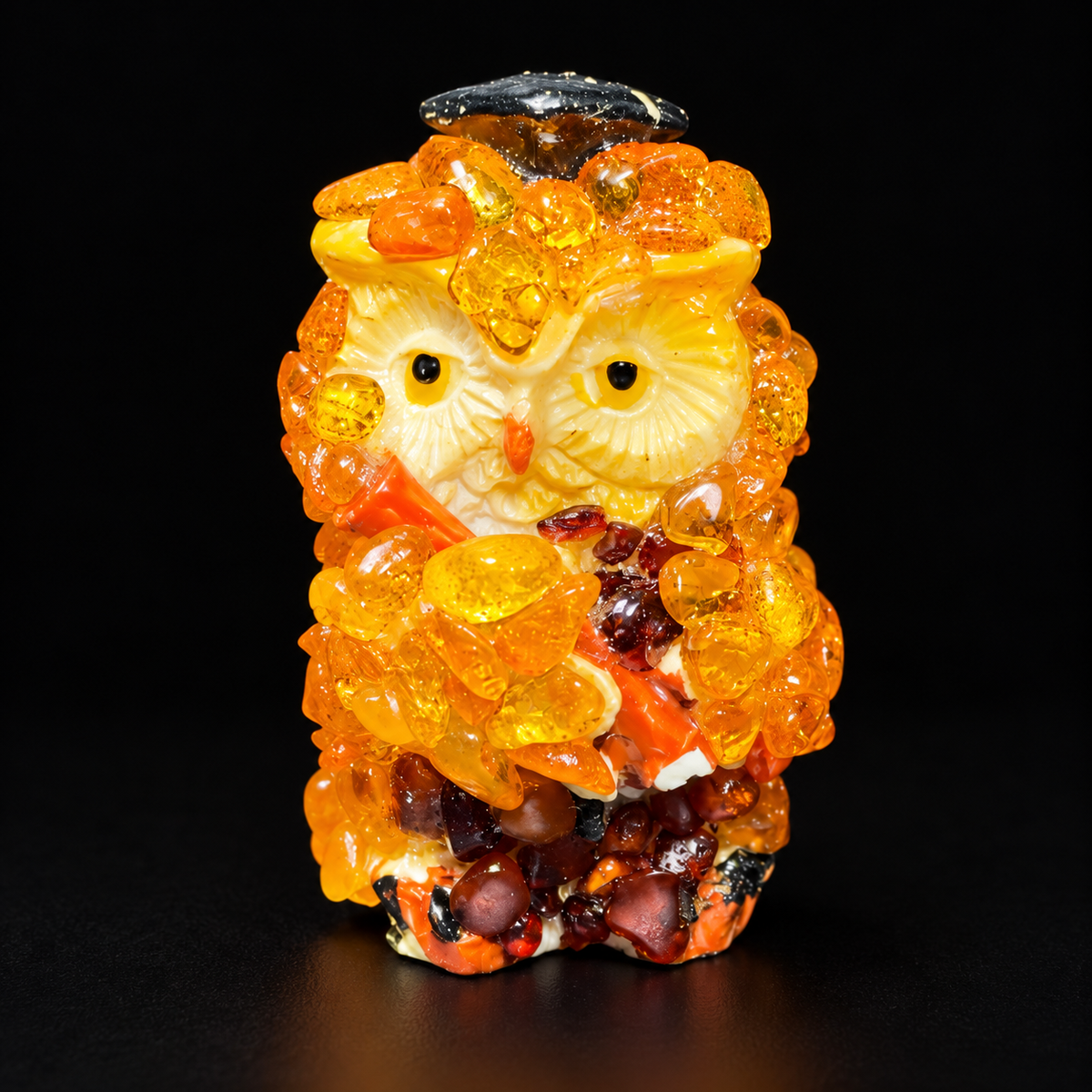 Golden graduation owl figurine with cream facial discs against a black background.