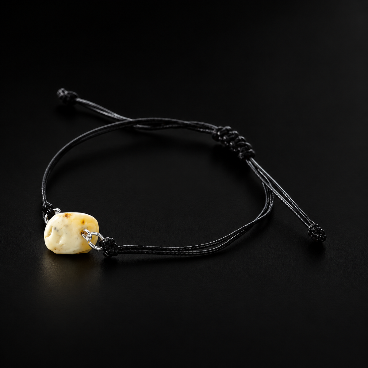 KIZIMA cream amber nugget on adjustable black cord bracelet on black studio background.