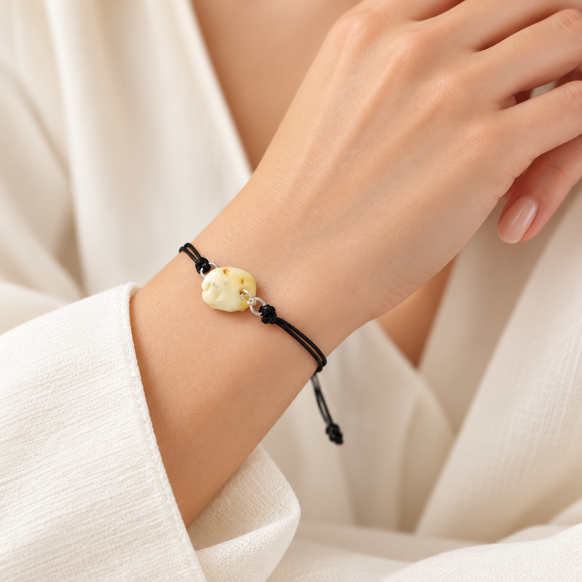 KIZIMA cream amber nugget on adjustable black cord bracelet on a young adult woman's wrist.