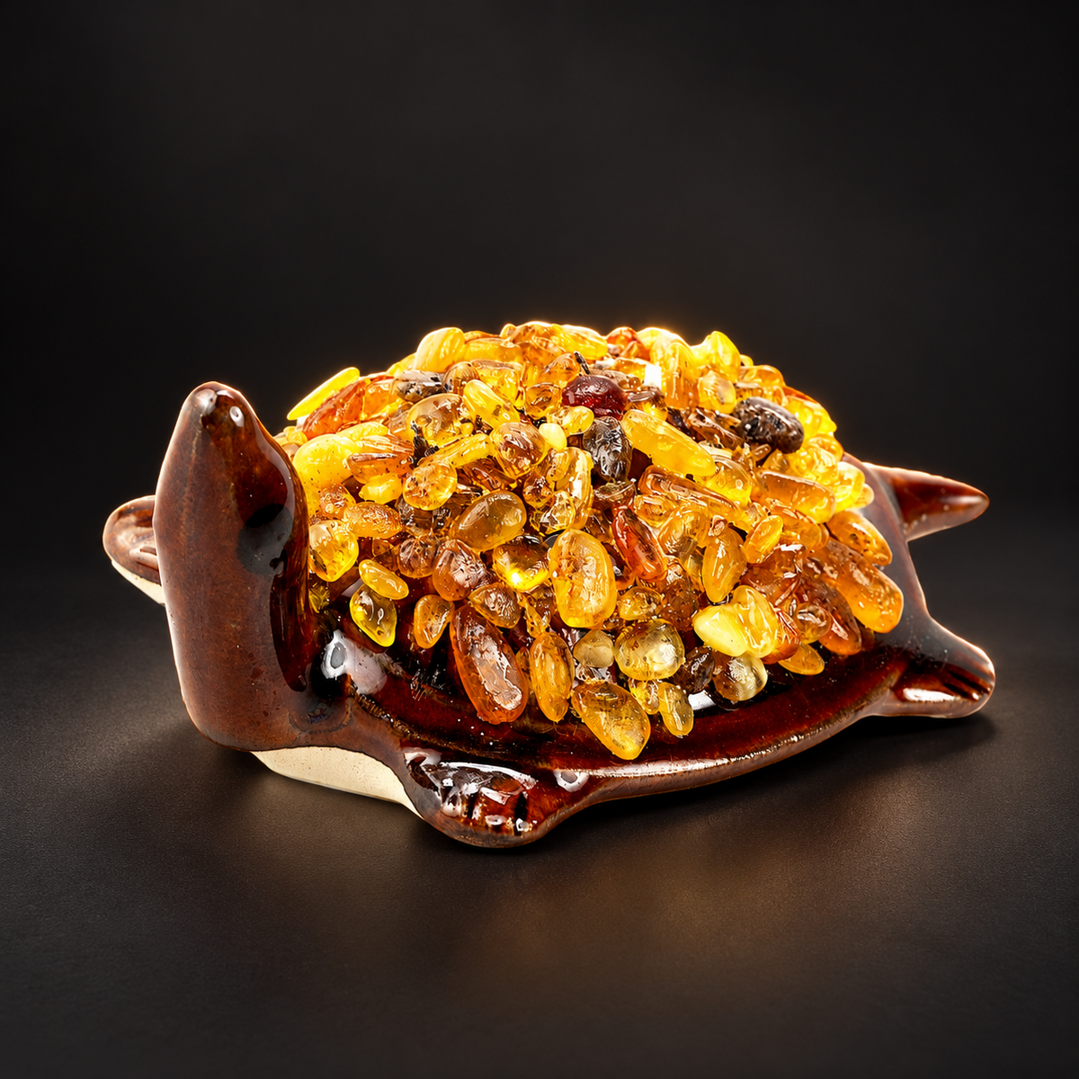 KIZIMA 10N0050q21 Baltic amber turtle figurine on a black studio background, showing the brown ceramic body and natural amber-chip shell.