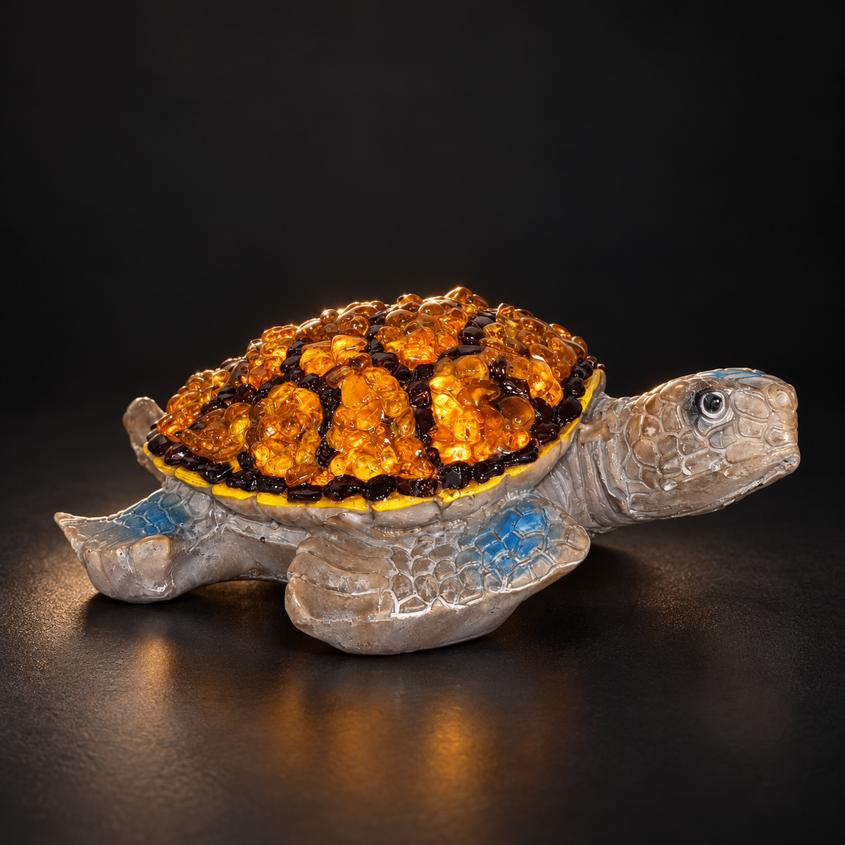 KIZIMA 5599170T Baltic amber turtle figurine on a black studio background, showing the grey sea-turtle body, blue accents and amber mosaic shell.