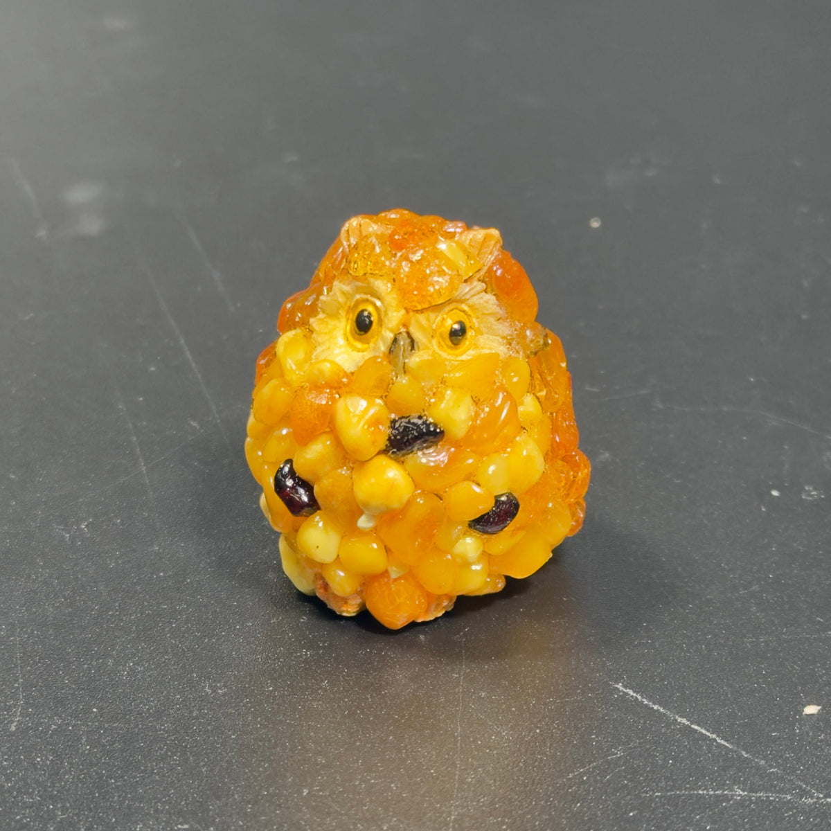 Original photograph of the yellow-orange owl figurine with dark accents on a gray surface