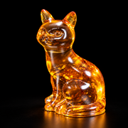 KIZIMA cognac amber sitting cat, 11 cm, with natural transmitted amber light on a deep black studio background