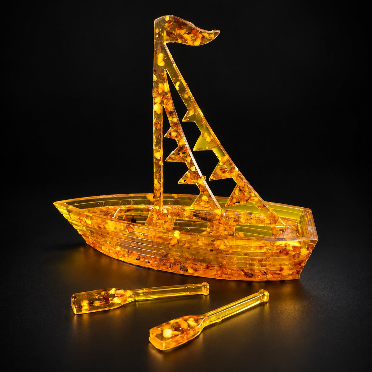 KIZIMA amber sailboat with flags sail and two oars, illuminated against a black studio background.