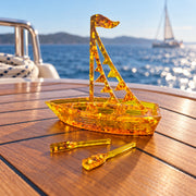 KIZIMA flags sailboat miniature and two amber oars on a teak yacht table with the blue sea behind.