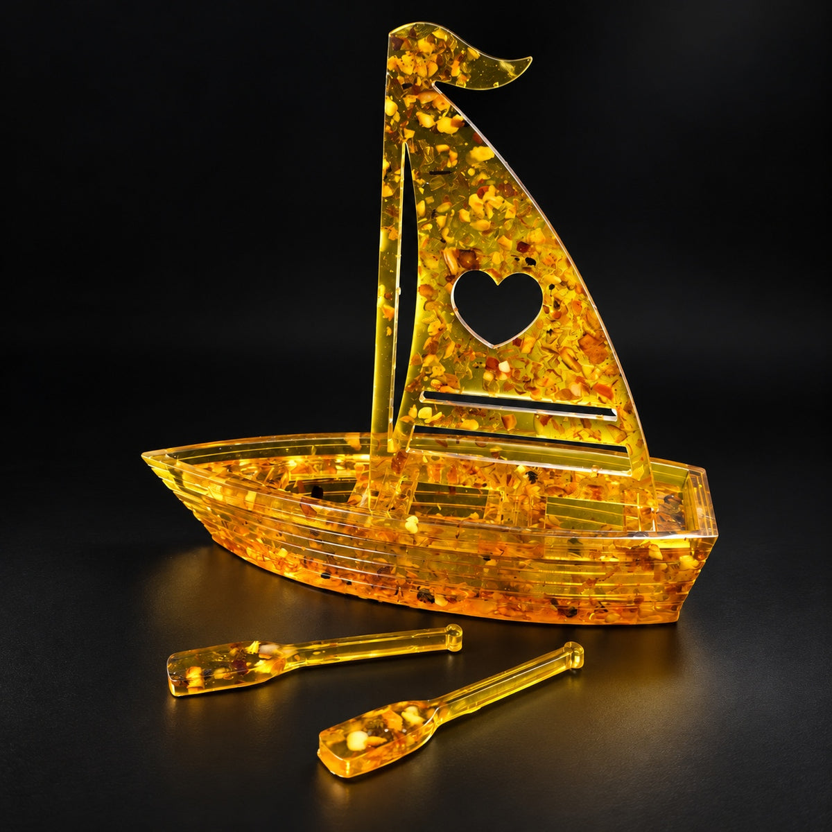KIZIMA amber sailboat with heart sail and two oars, illuminated against a black studio background.