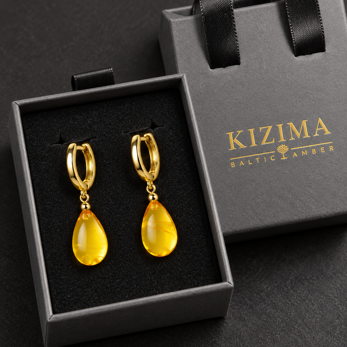 KIZIMA golden amber teardrop earrings on gold-tone hoops presented in the gray KIZIMA Baltic Amber ribbon-handle gift box.