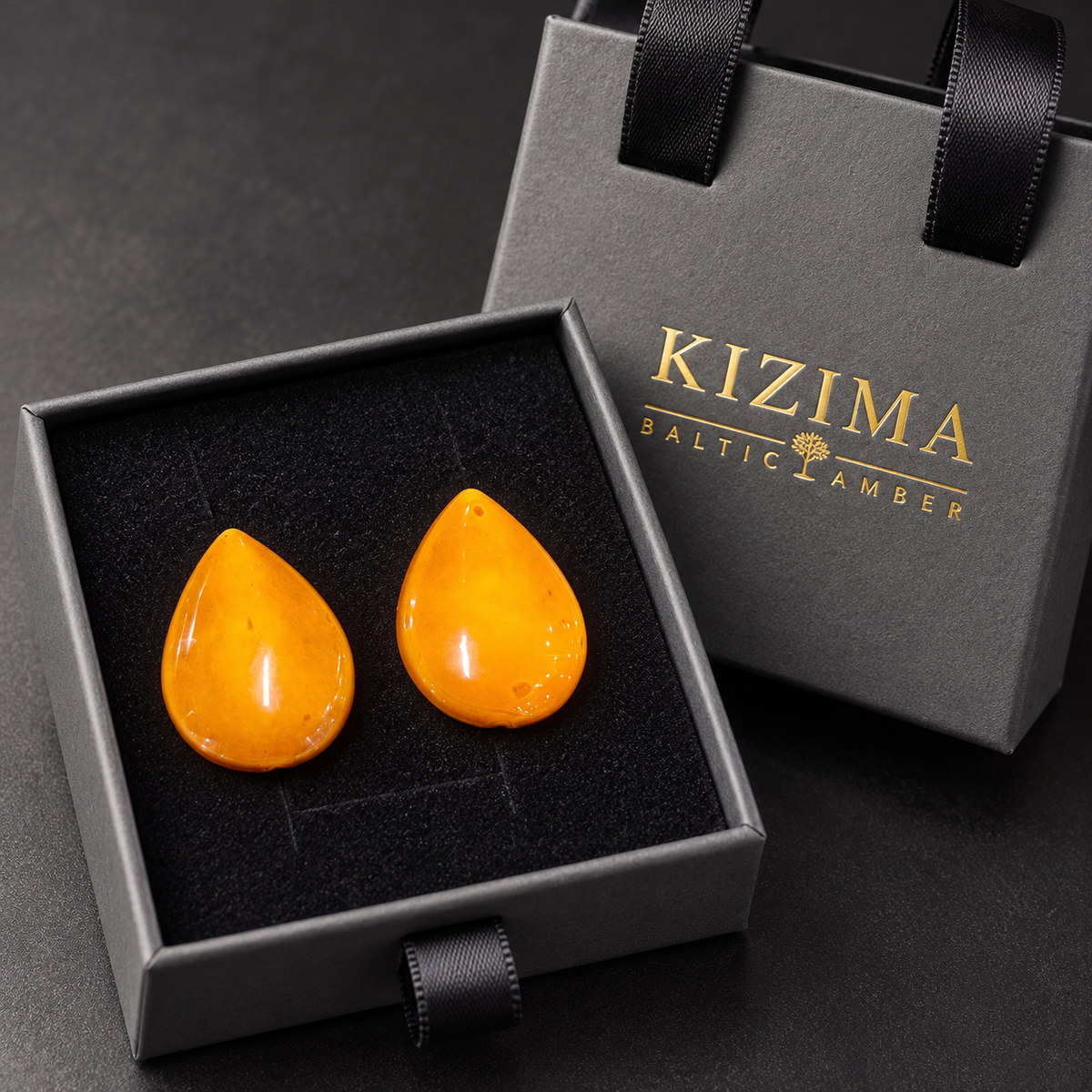 KIZIMA vintage honey-orange amber teardrop studs displayed on the black insert of the gray KIZIMA Baltic Amber gift box.