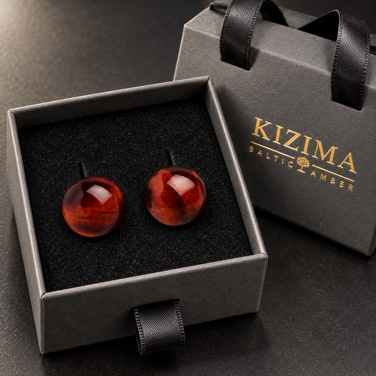 Dark cognac amber stud earrings in a charcoal gray KIZIMA ribbon-handle gift box with black insert.