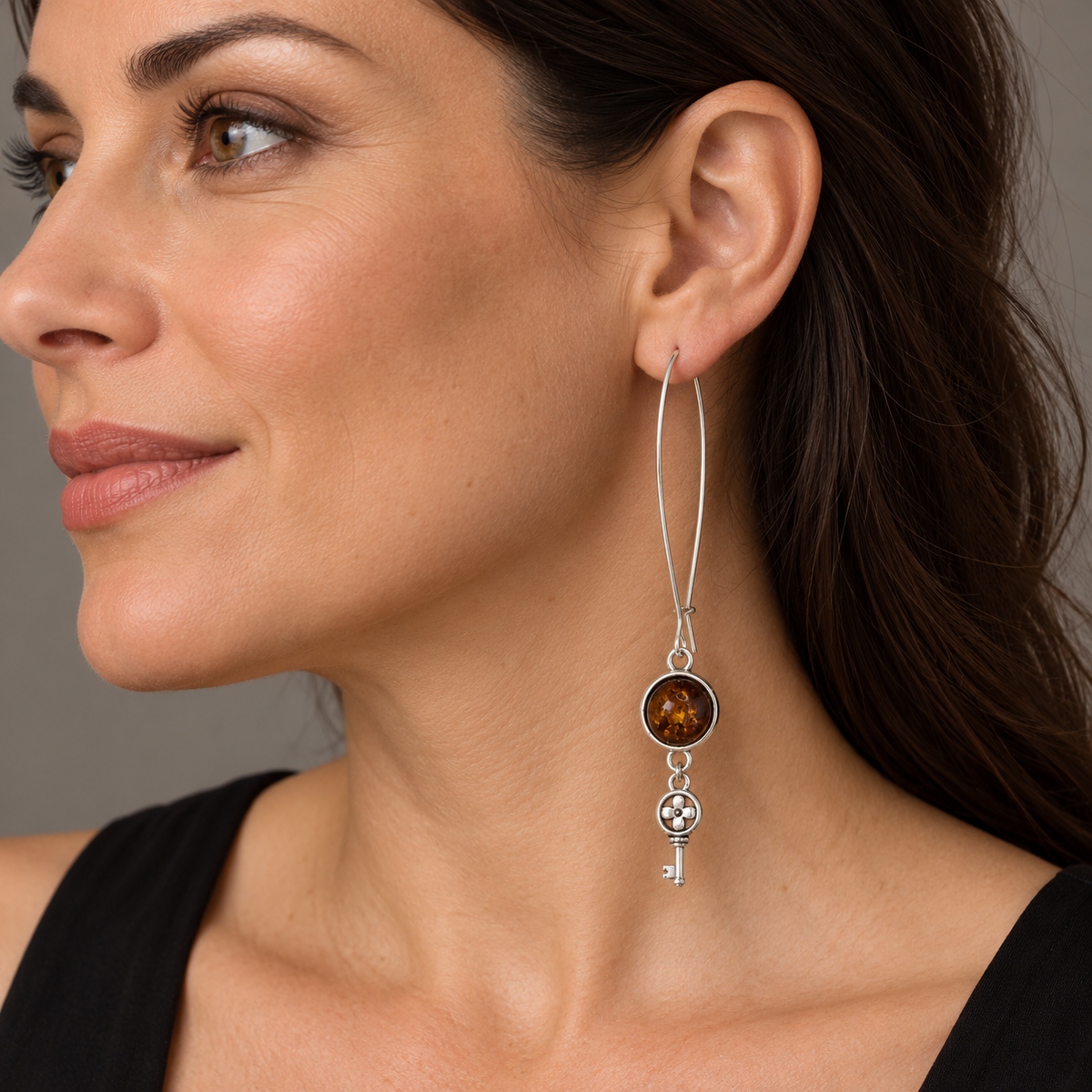 Adult woman wearing a long KIZIMA cognac amber earring with a slender marquise wire and floral key charm.