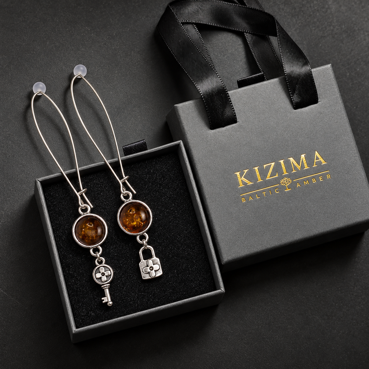 KIZIMA extra-long silver wire cognac amber key and lock earrings presented with the gray KIZIMA Baltic Amber gift box.