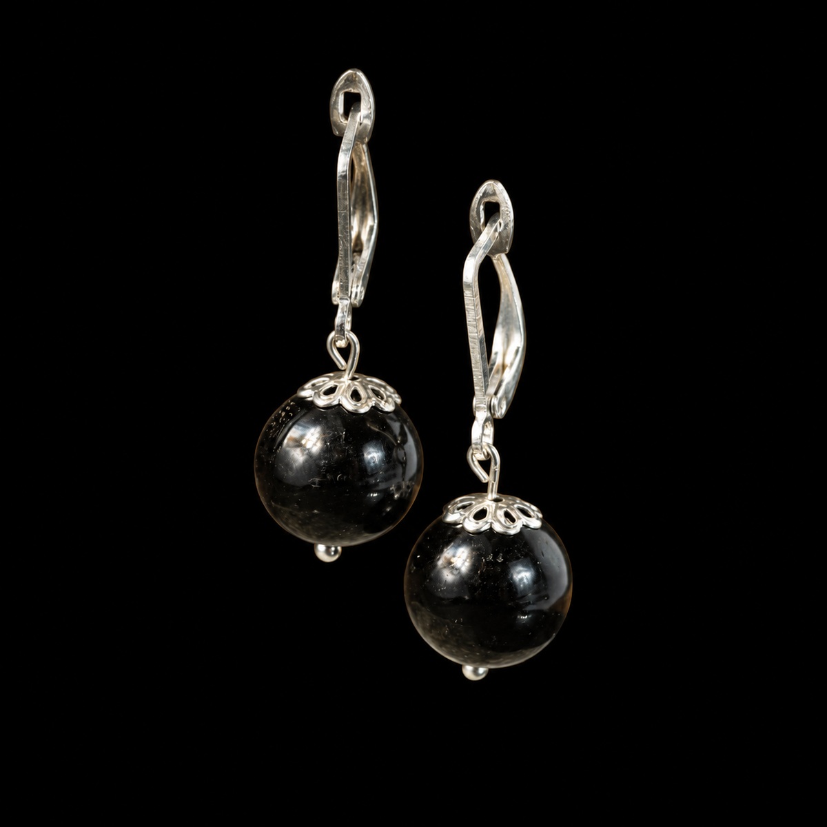 KIZIMA black Baltic amber sphere earrings with silver-tone leverbacks and filigree caps on a black studio background