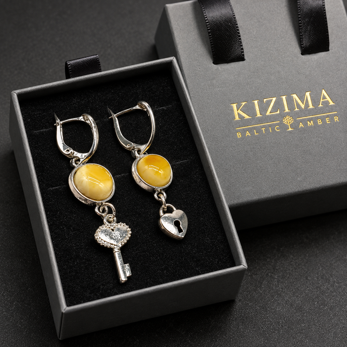 KIZIMA yellow amber key and heart-lock leverback earrings displayed on black velvet with the gray KIZIMA Baltic Amber ribbon-handle gift box.