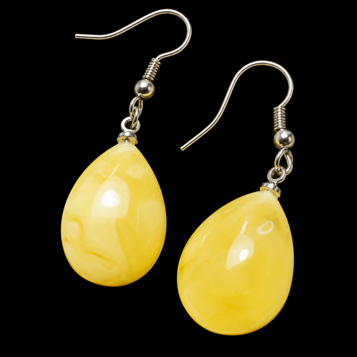 KIZIMA butter-yellow Baltic amber teardrop earrings with silver-tone fishhooks on a black studio background