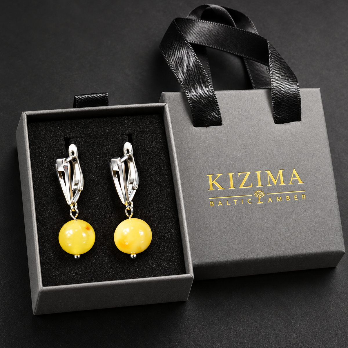 Opaque yellow amber ball earrings in a charcoal gray KIZIMA ribbon-handle gift box with black insert.