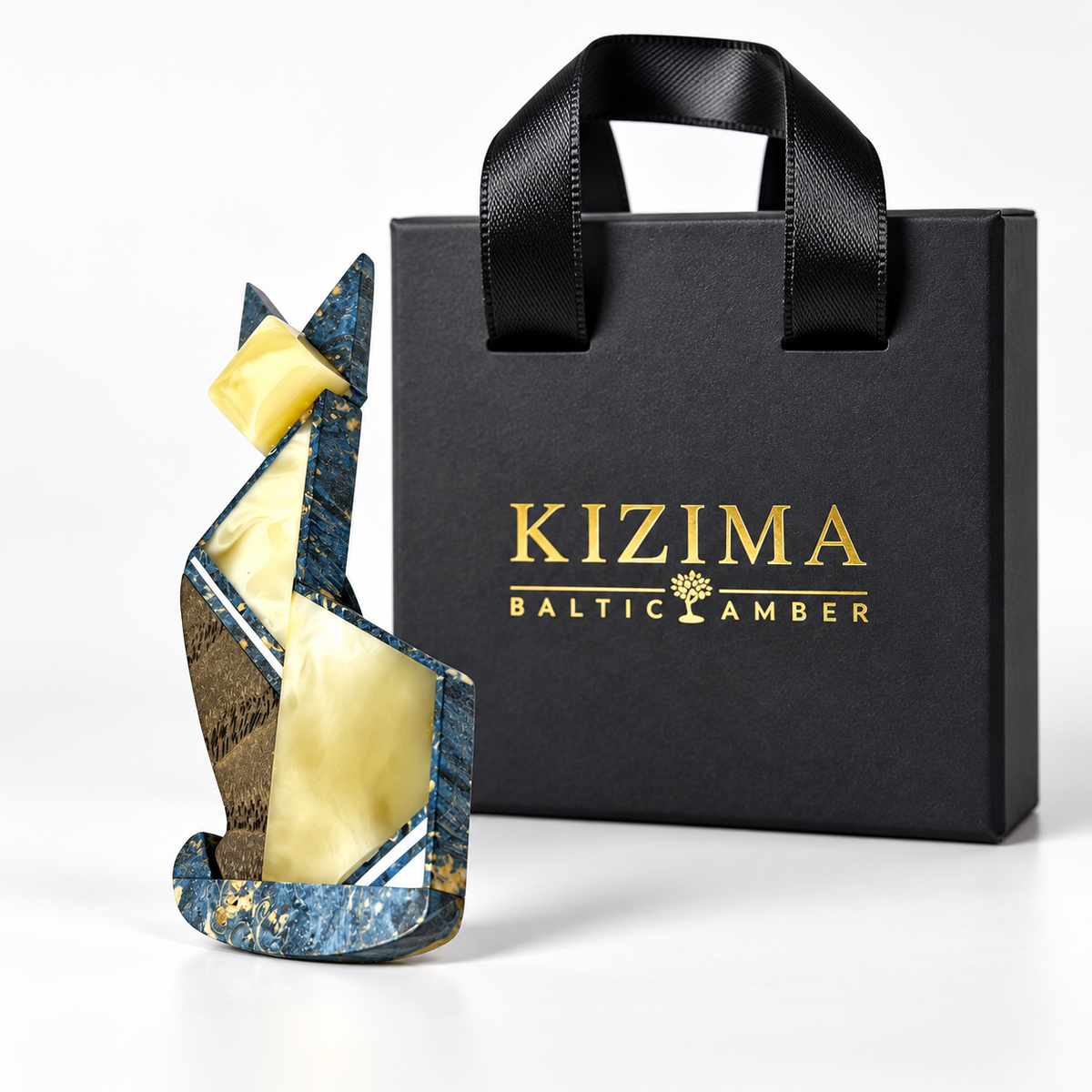 Blue and yellow geometric cat brooch displayed beside black KIZIMA gift packaging.