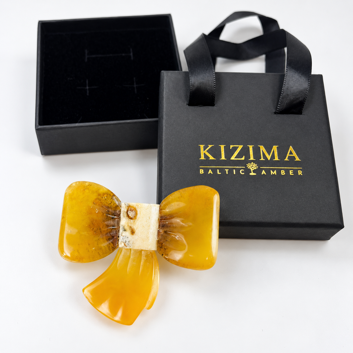 KIZIMA amber bow brooch beside black KIZIMA gift packaging.