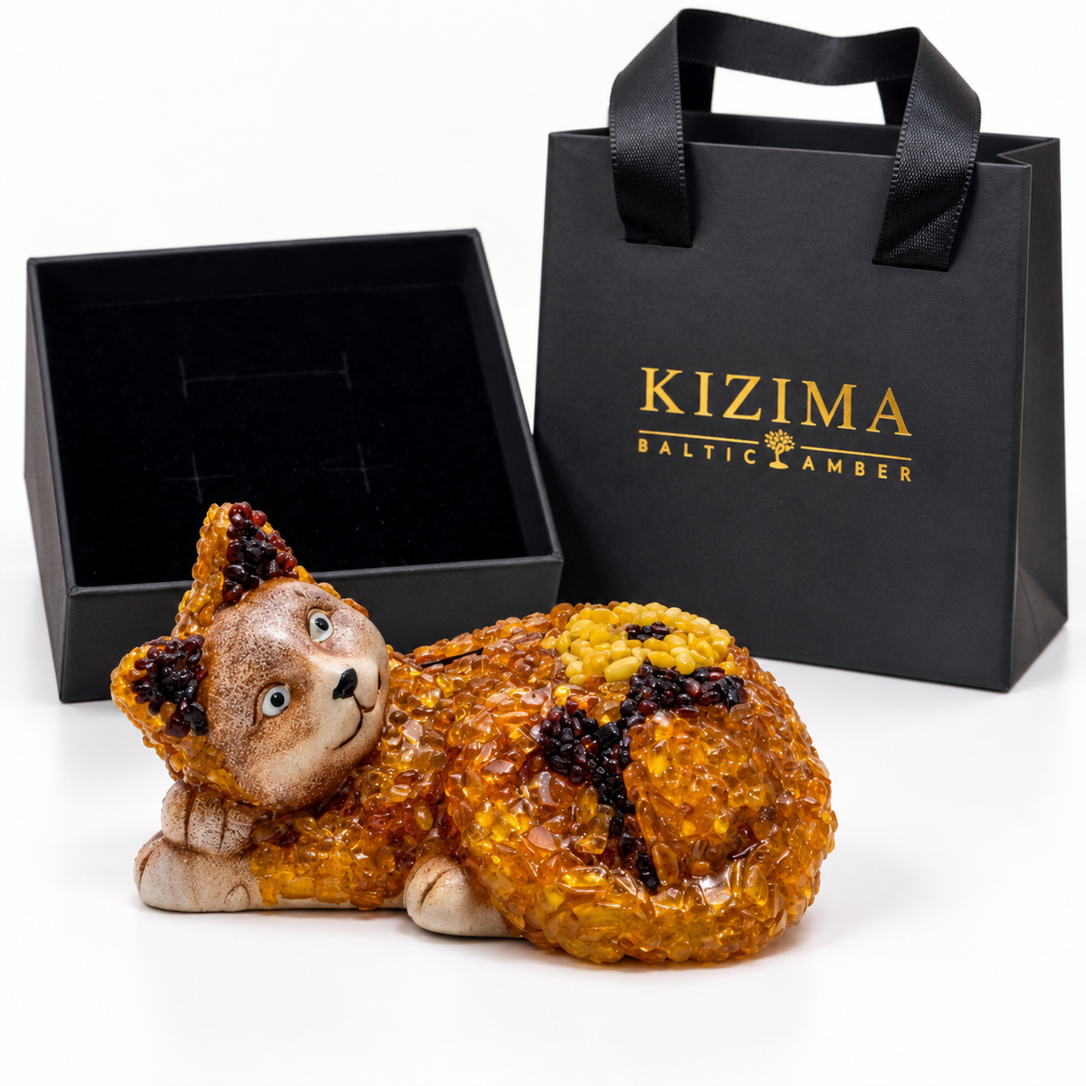 Reclining cat money box beside an open black velvet-lined box and branded KIZIMA gift bag