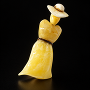 KIZIMA Baltic amber lady brooch 20S1974q6.58 on a deep black studio background, front view with cream hat and marbled flowing skirt