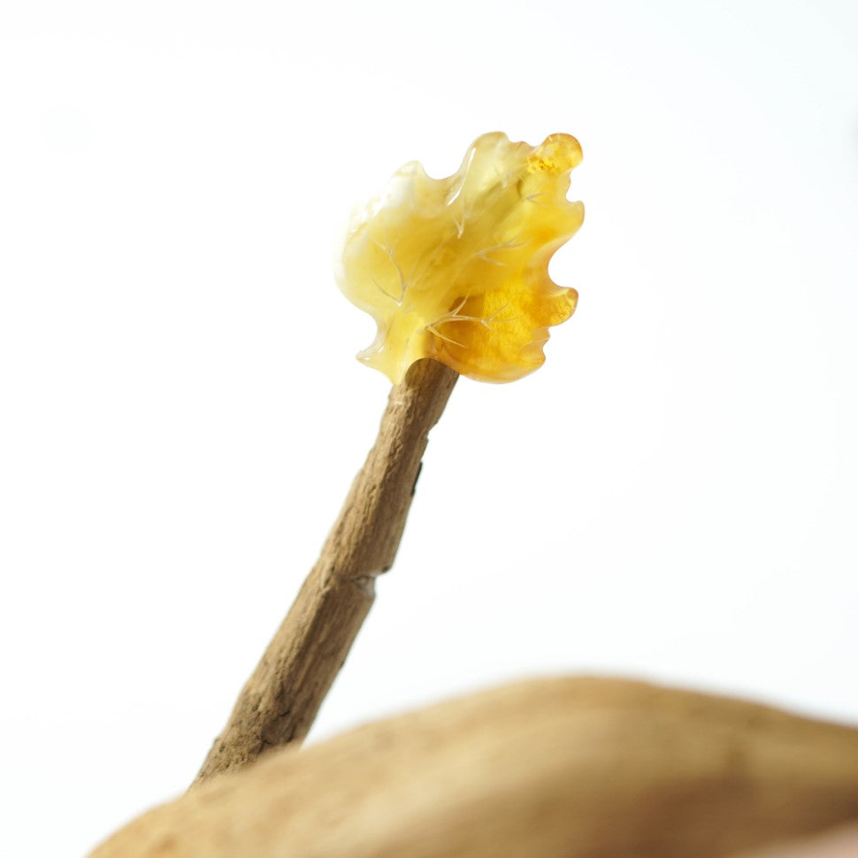 Carved yellow amber leaf brooch displayed on a natural branch against a light background; a Christmas gift for a gardener.