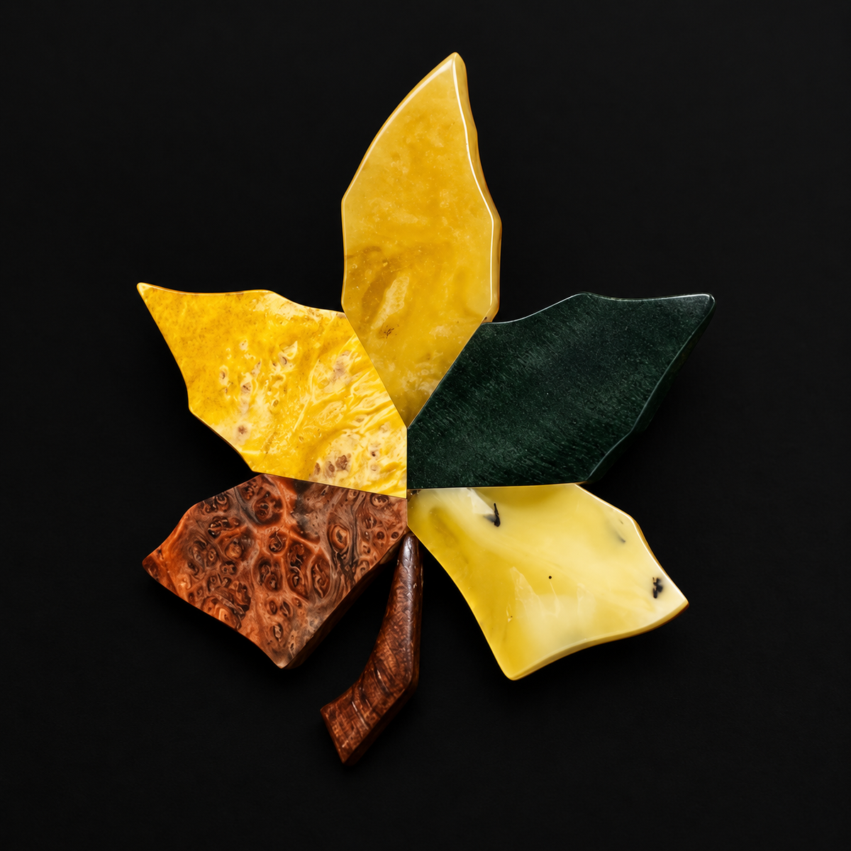 Close-up of a maple leaf brooch showing yellow amber, dark green wood and brown figured grain against black.
