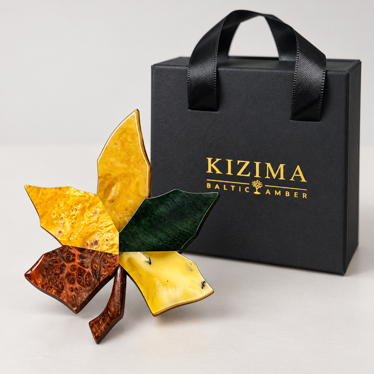 Multicolored maple leaf brooch displayed beside black KIZIMA gift packaging.