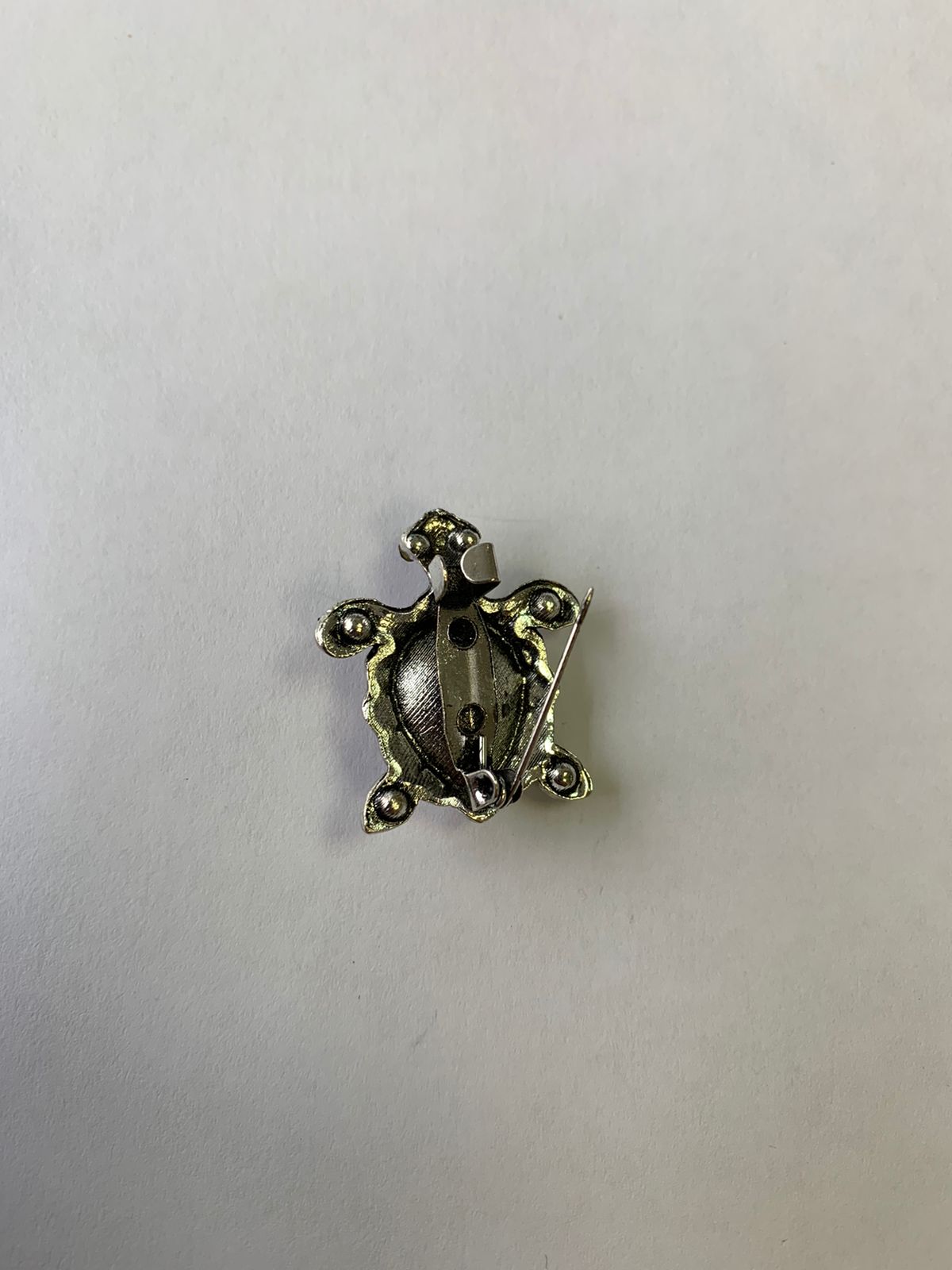 Back of an amber turtle brooch with its metal pin open on a pale surface; a birthday gift for a turtle lover.