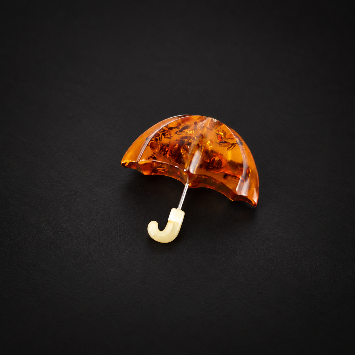 Cognac amber umbrella brooch with visible natural inclusions on a black studio surface.
