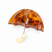 Amber umbrella brooch with a carved cognac canopy and cream hook handle on a white background.
