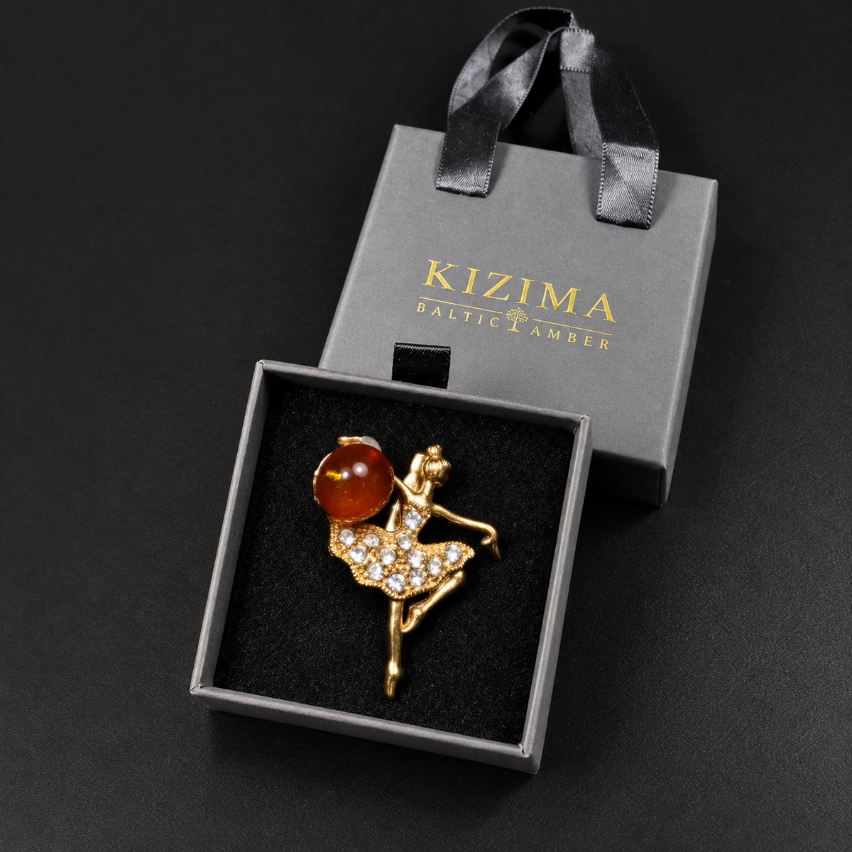 KIZIMA gold-tone Baltic amber ballerina brooch 20N0120-7 inside the charcoal-gray KIZIMA velvet-lined drawer gift box beside its ribbon-handled outer sleeve