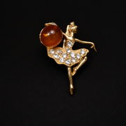 KIZIMA gold-tone Baltic amber ballerina brooch 20N0120-Group3 on a deep black studio background, with round cognac amber and clear rhinestone tutu