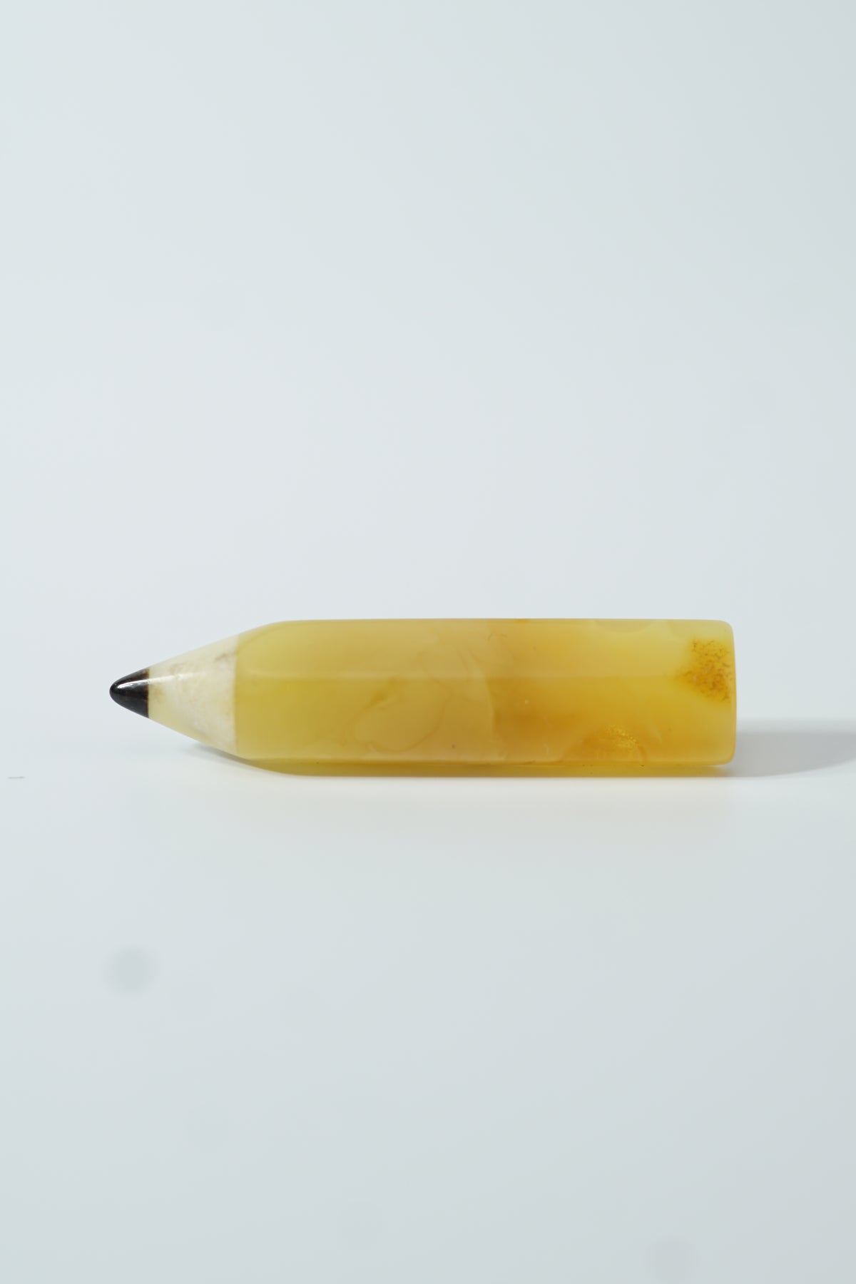 Yellow Baltic amber pencil brooch with a faceted body and dark tip on a pale surface; a Teacher Appreciation gift.