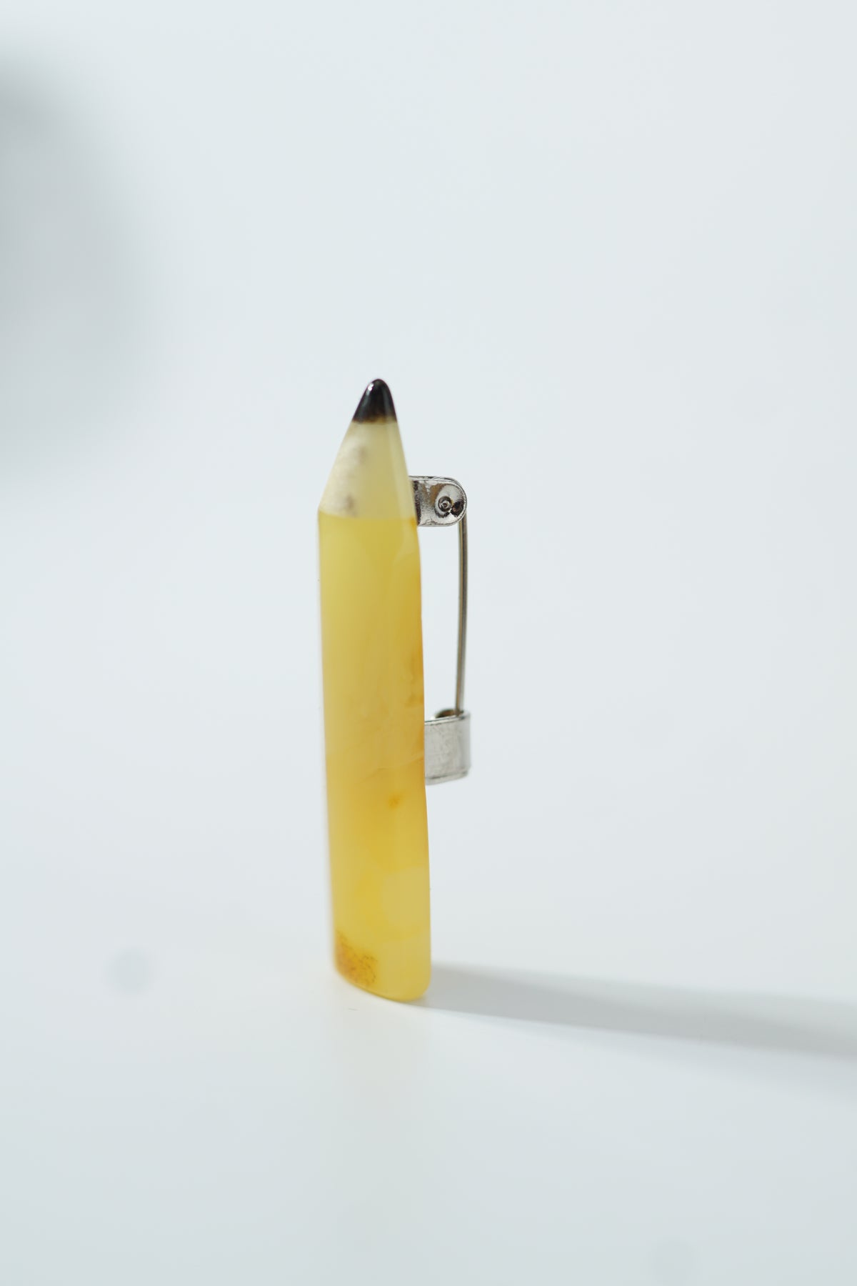 Side view of a yellow amber pencil brooch showing its dark tip and metal pin; a Christmas gift for a teacher.