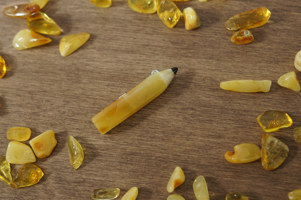 Yellow amber pencil brooch on wood surrounded by amber pieces; a birthday gift for a writer or artist.