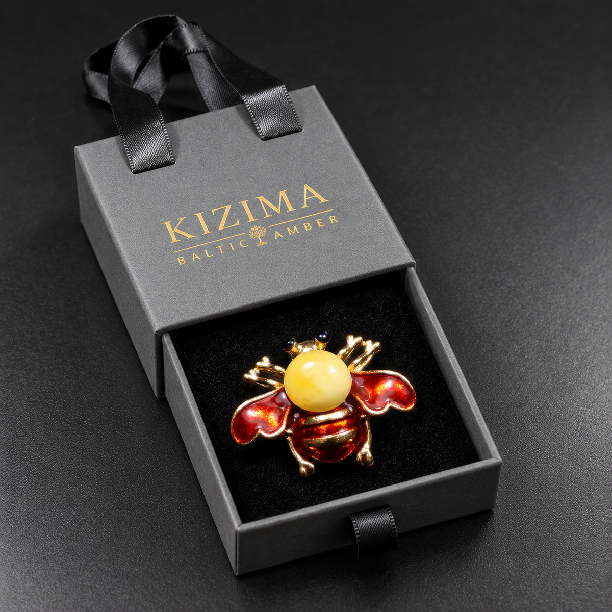 KIZIMA red enamel and opaque pale-yellow Baltic amber bee brooch 20-305Q5-3-3-2 in its charcoal-gray KIZIMA velvet-lined drawer gift box.