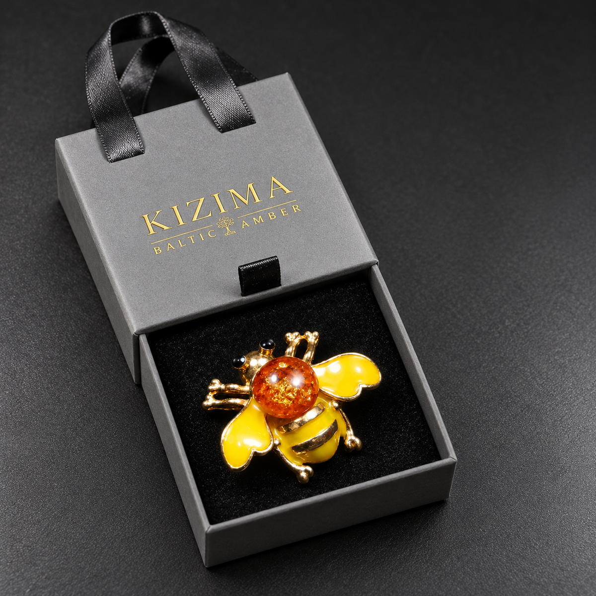 KIZIMA yellow enamel and cognac Baltic amber bee brooch 20-306Q5-3-3-2 in its charcoal-gray KIZIMA velvet-lined drawer gift box.