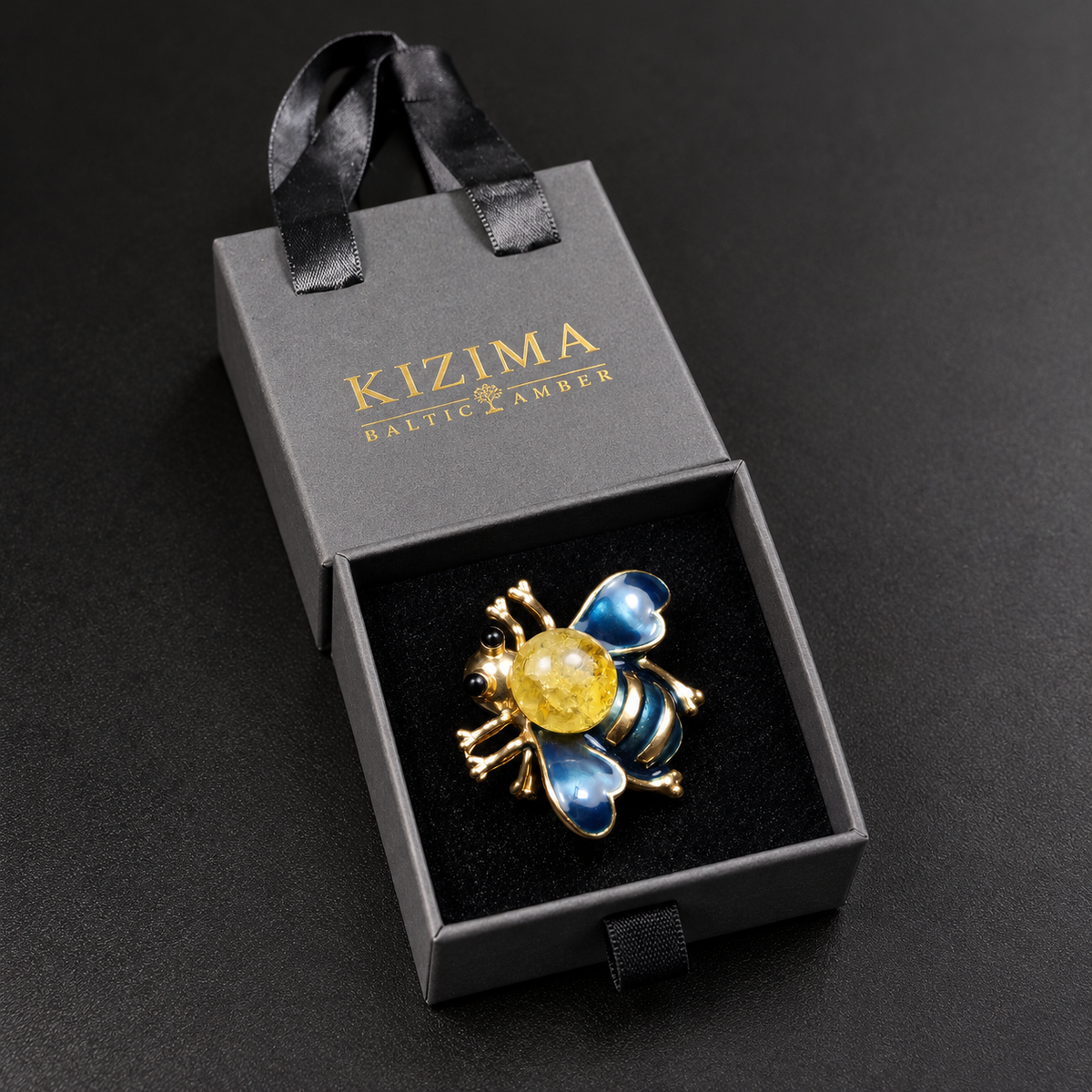 KIZIMA blue enamel and lemon Baltic amber bee brooch 20-308Q5-3-3-2 in its charcoal-gray KIZIMA velvet-lined drawer gift box.