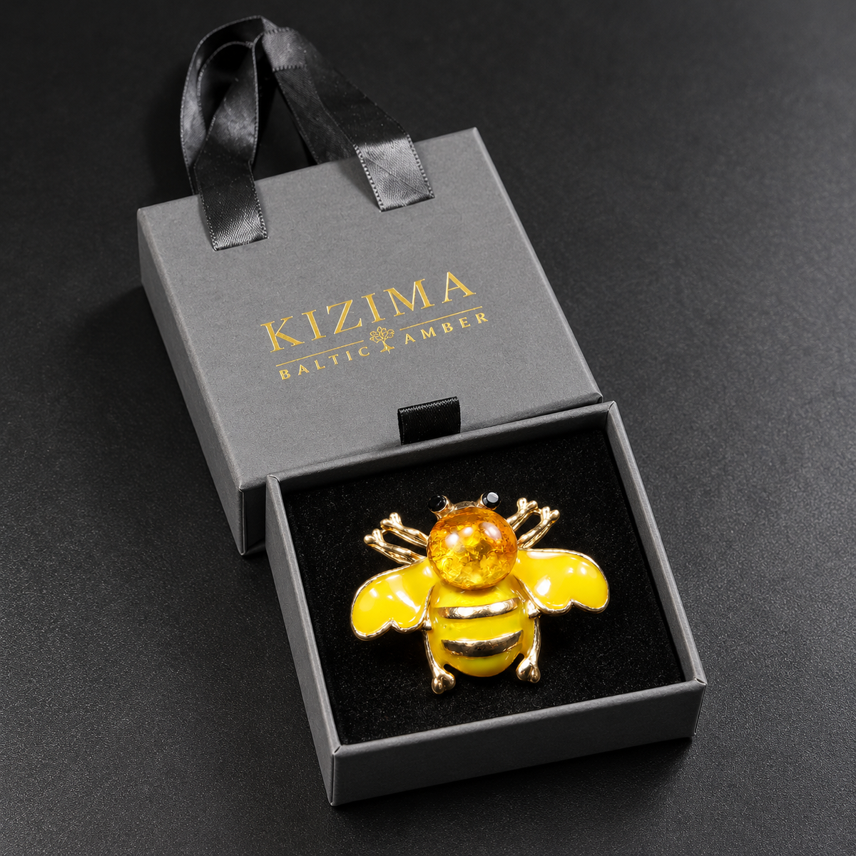 KIZIMA yellow enamel bee brooch 20N0120-35 with round Baltic amber in its charcoal-gray KIZIMA velvet-lined drawer gift box.