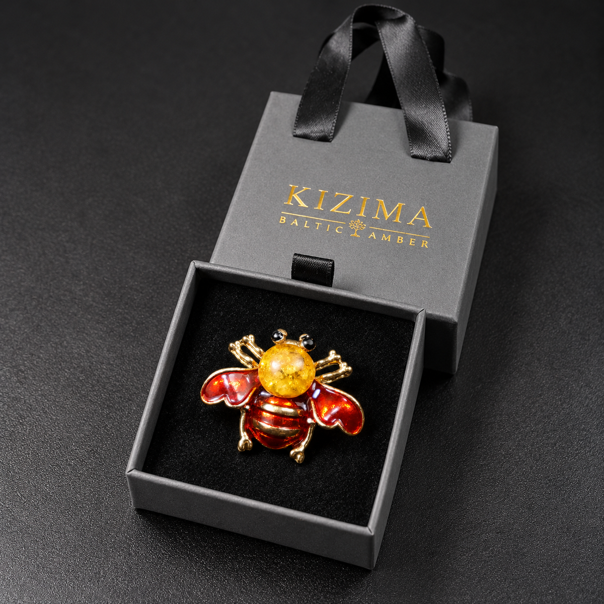 KIZIMA red enamel bee brooch 20N0120-36 with round Baltic amber in its charcoal-gray KIZIMA velvet-lined drawer gift box.