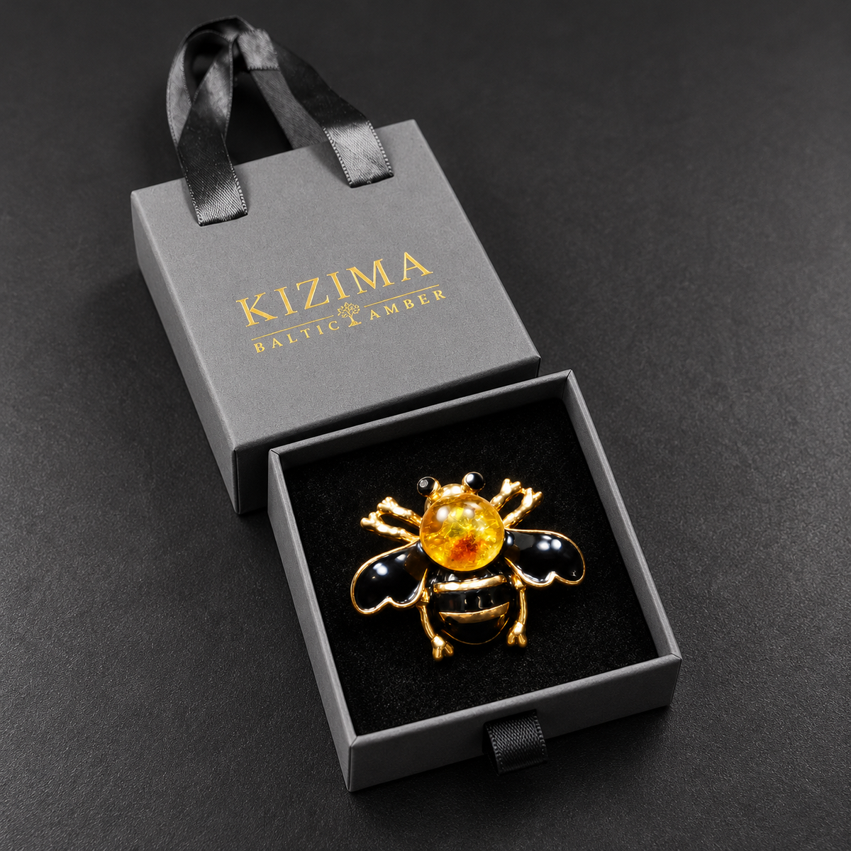 KIZIMA black enamel bee brooch 20N0120-38 with round Baltic amber in its charcoal-gray KIZIMA velvet-lined drawer gift box.
