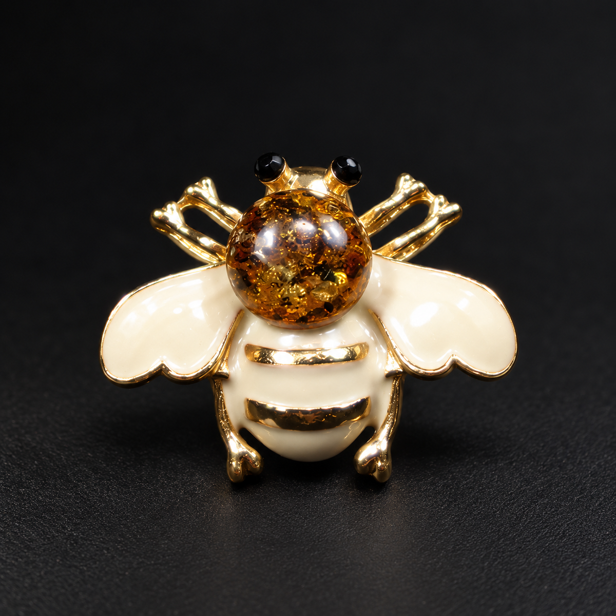 KIZIMA cream-white enamel bee brooch 20N0120-39 with round Baltic amber on a black studio background.