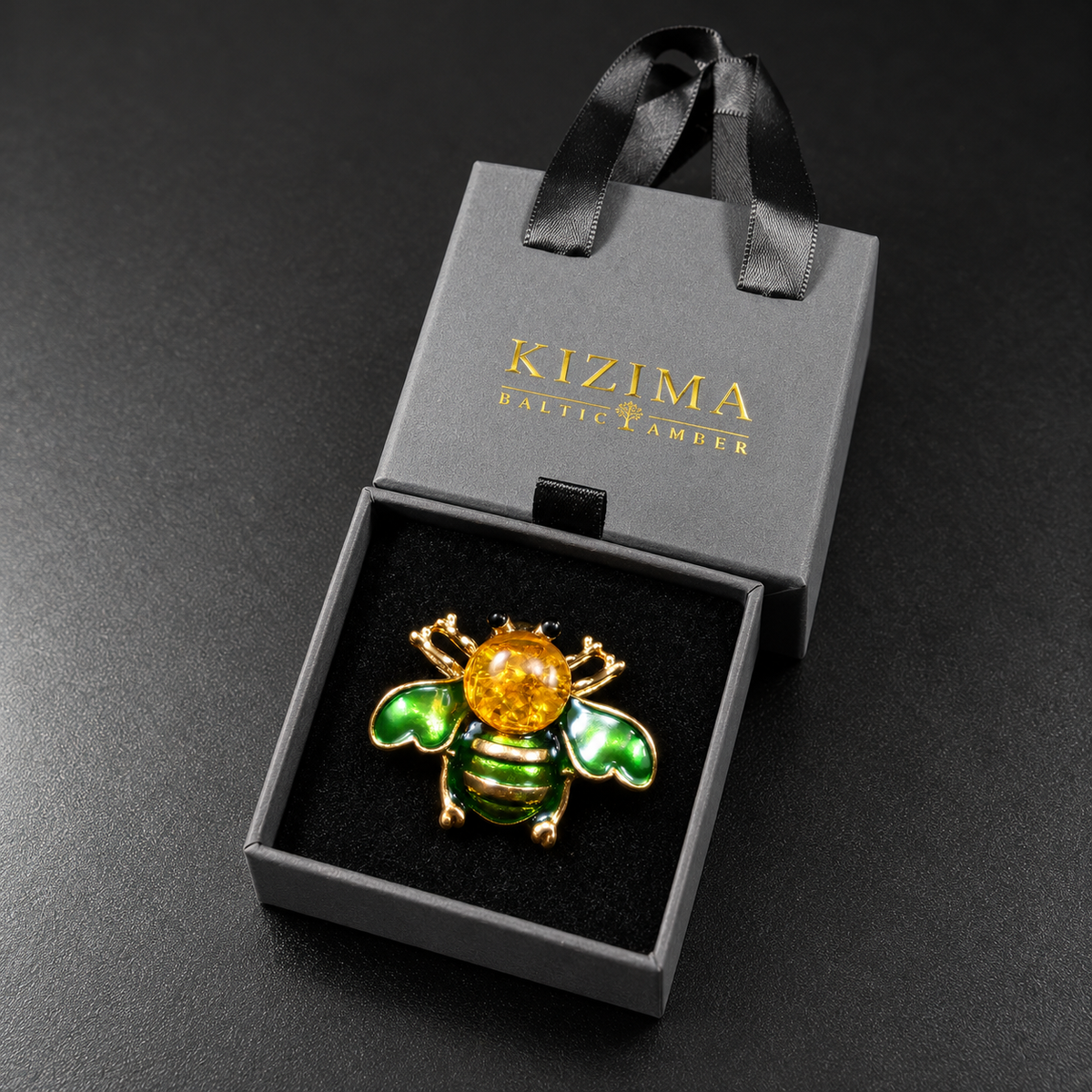 KIZIMA green enamel bee brooch 20N0120-40 with round Baltic amber in its charcoal-gray KIZIMA velvet-lined drawer gift box.