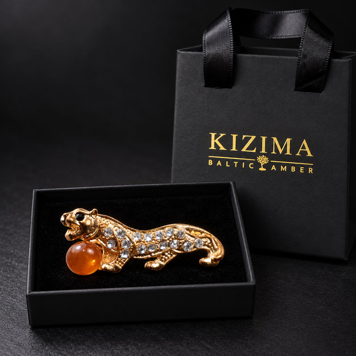 KIZIMA gold-tone tiger brooch 20N0120-19 with honey-orange Baltic amber in the real black velvet KIZIMA box beside the matching gift bag.
