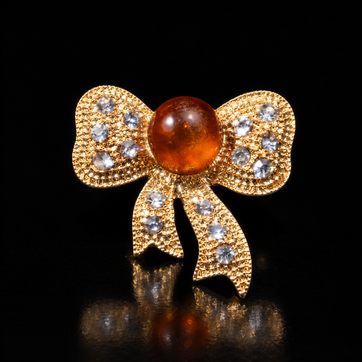 KIZIMA gold-tone bow brooch 20N0120-23 with honey-orange Baltic amber on a black studio background.
