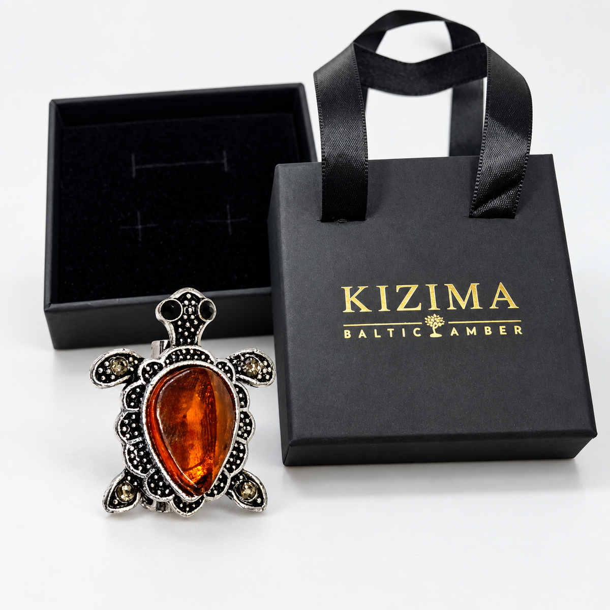 KIZIMA Baltic amber brooch 20N0180-8 beside authentic black KIZIMA gift packaging.