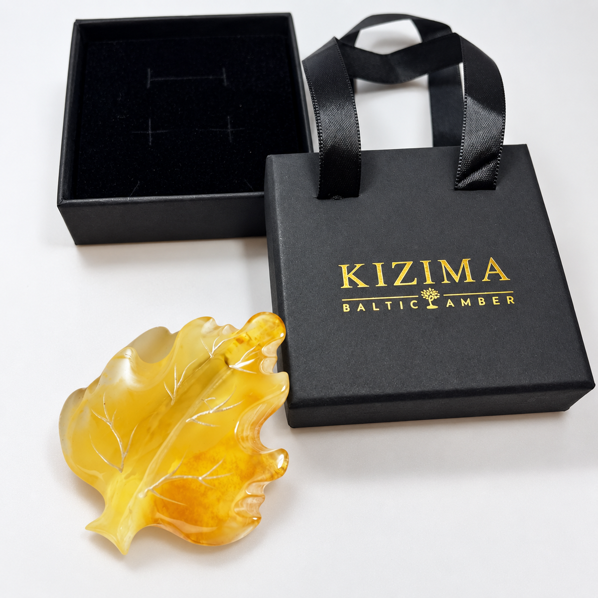 KIZIMA Baltic amber brooch 20S0900q3.00 beside authentic black KIZIMA gift packaging.